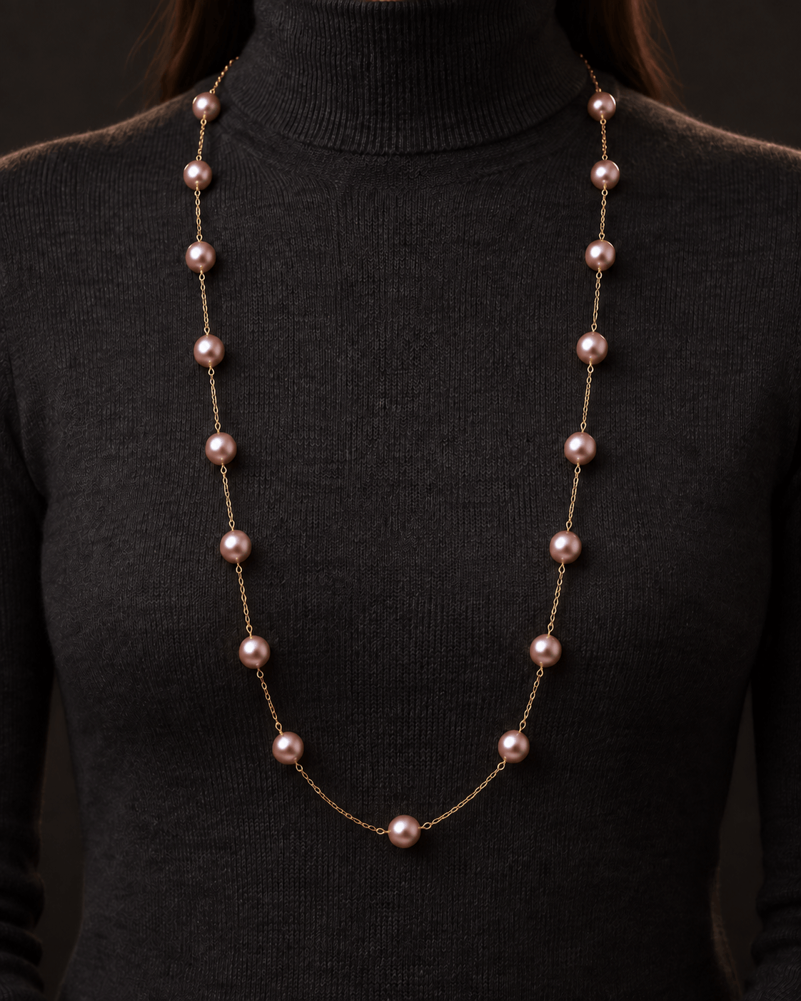 A long necklace with pink freshwater pearls on a delicate gold chain, shown worn on a person's neck over a black turtleneck sweater.