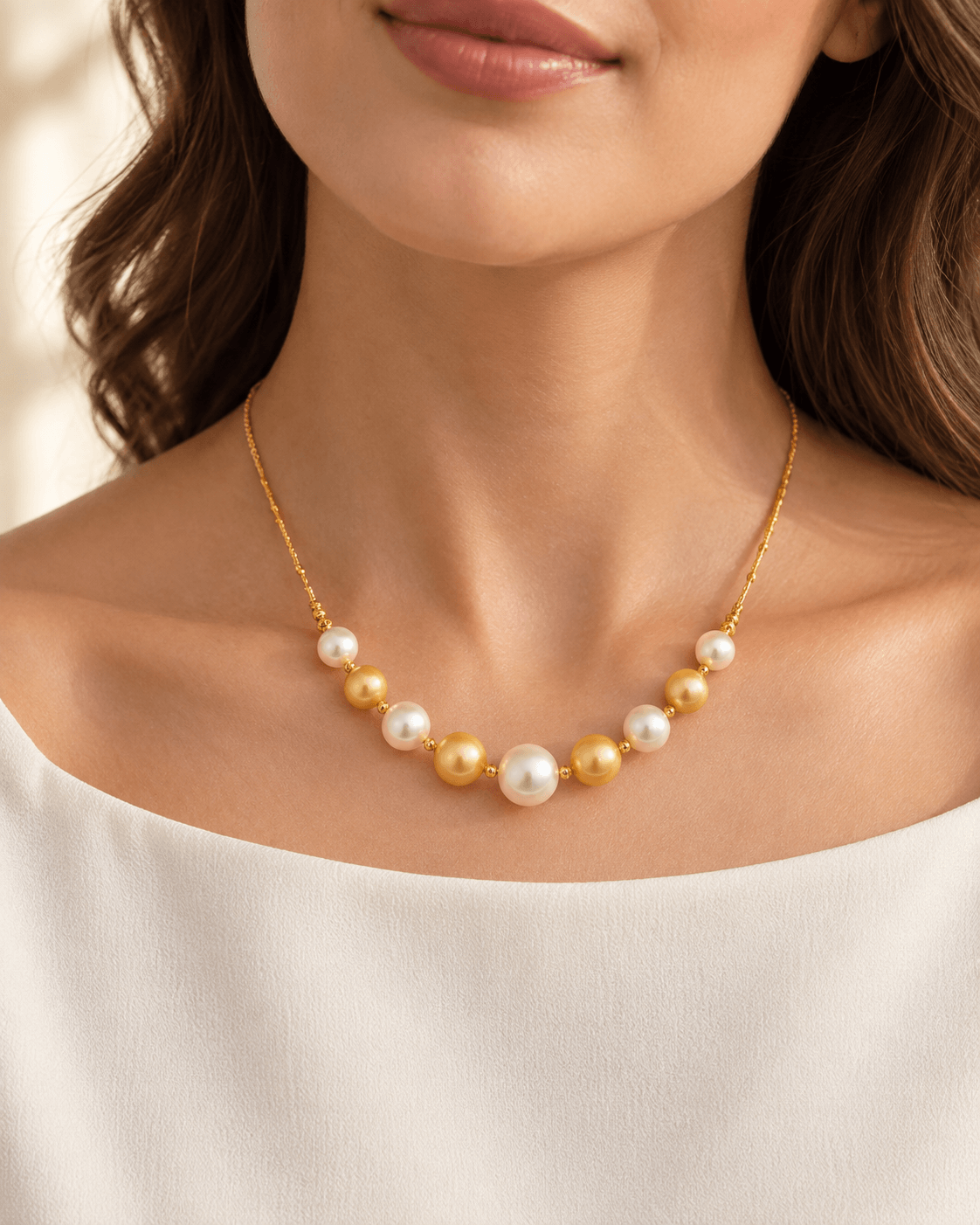 A close-up of a woman wearing a delicate gold necklace with alternating white and gold pearls, styled with a white off-the-shoulder top.