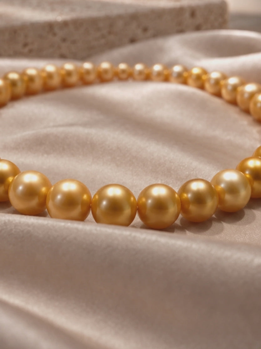 Golden South Sea style pearl necklace strand with warm metallic luster on champagne silk.