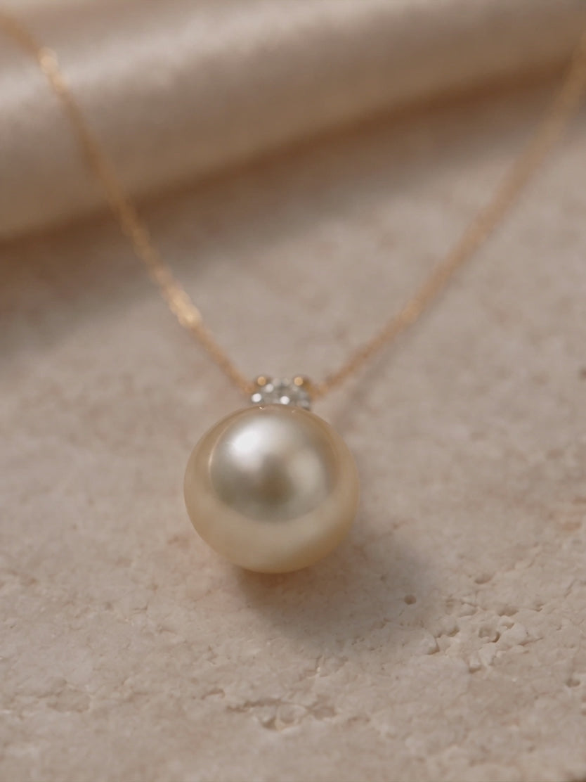 Close-up of a golden pearl pendant necklace with diamond accents on a delicate gold chain.