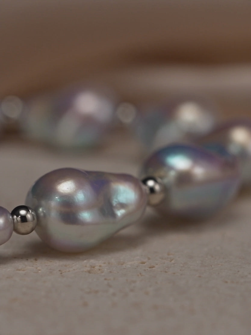 Macro video showcasing the iridescent luster of an organic baroque pearl necklace accented with polished silver beads.