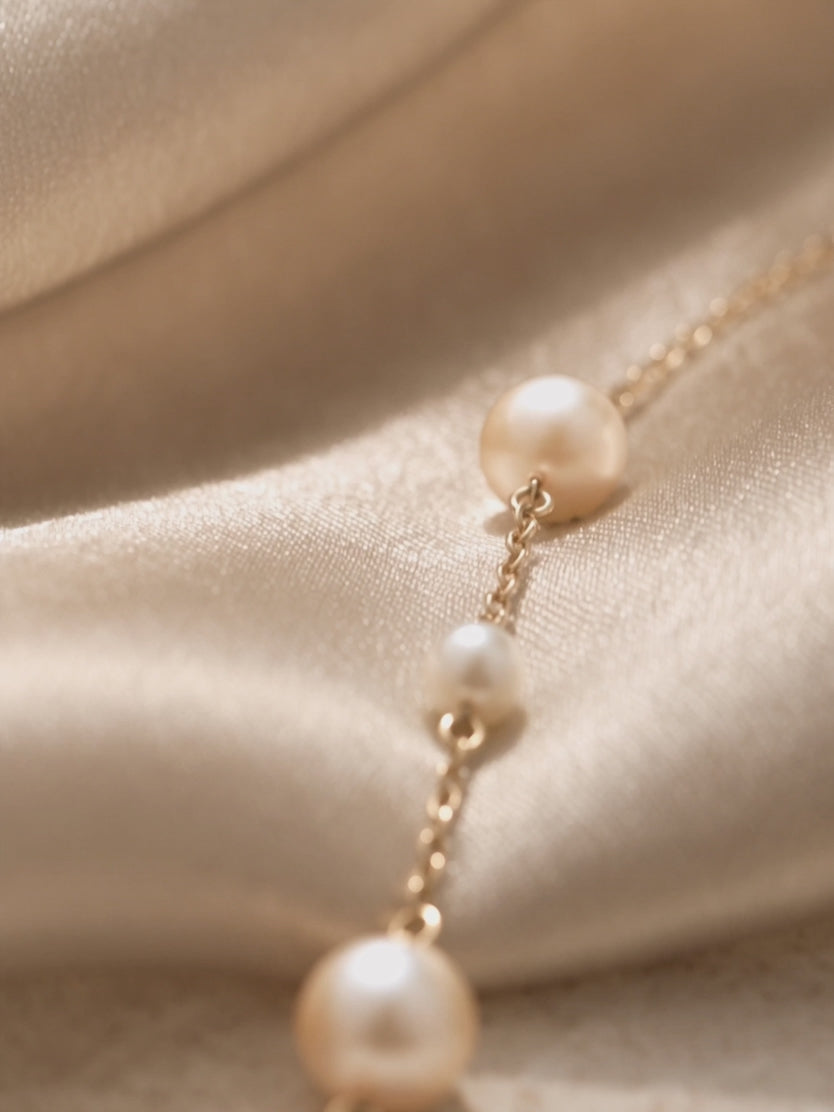 Anna Borjigin gold link necklace with alternating freshwater pearls displayed on champagne satin.