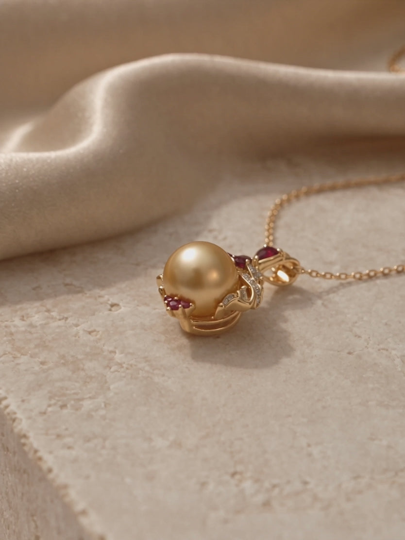 Golden pearl pendant necklace in a yellow gold setting with red gemstone and diamond accents.