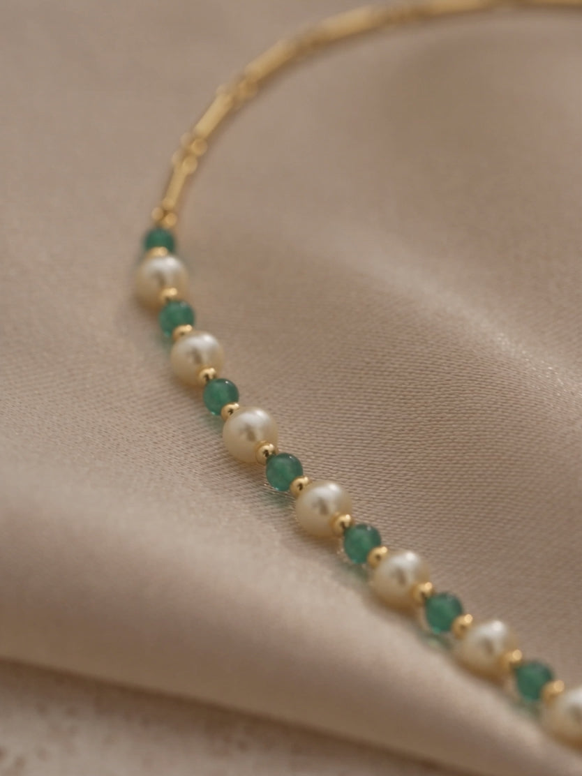 Anna Borjigin pearl and green gemstone necklace detail showcasing lustrous white pearls, faceted green beads, and gold chain links.