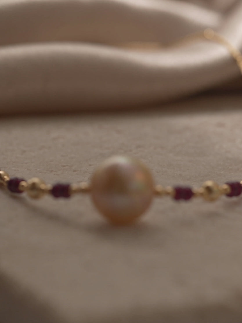 Handcrafted gold pearl necklace with a single central champagne pearl and ruby-red bead accents by Anna Borjigin.