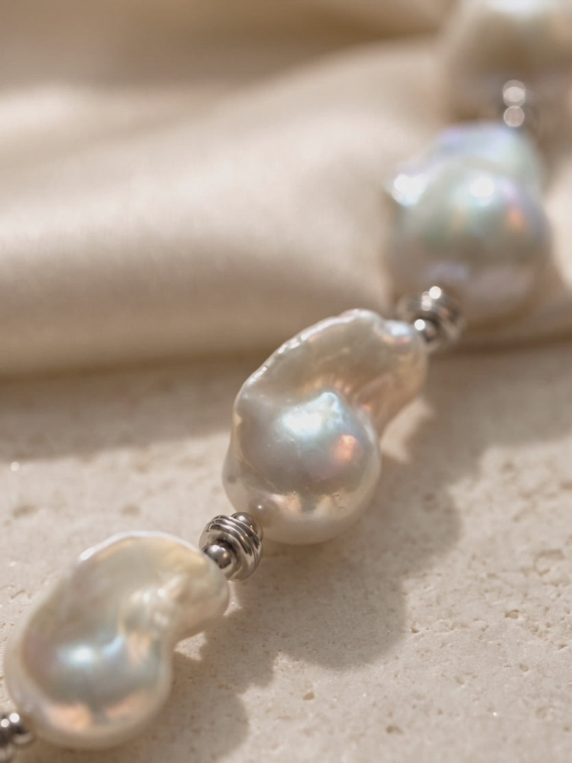 Handcrafted white baroque pearl necklace featuring organic-shaped pearls and silver spacer beads on a neutral stone background.